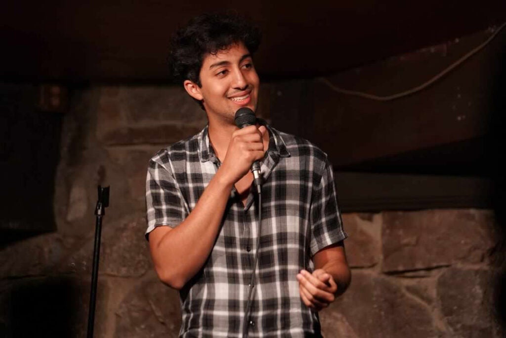 Zan Haq holds a microphone and stands on a stage.