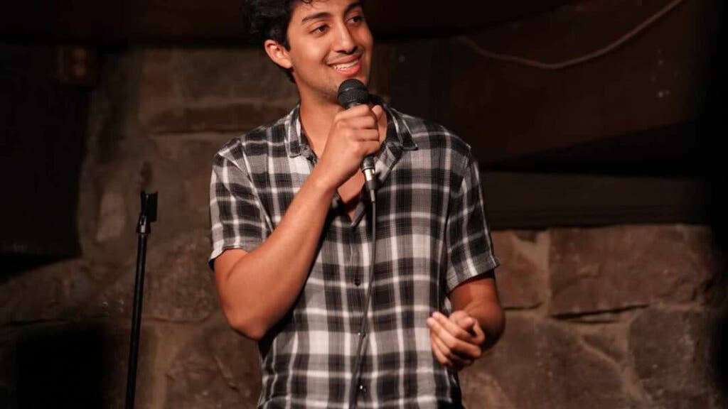 Zan Haq holds a microphone and stands on a stage.
