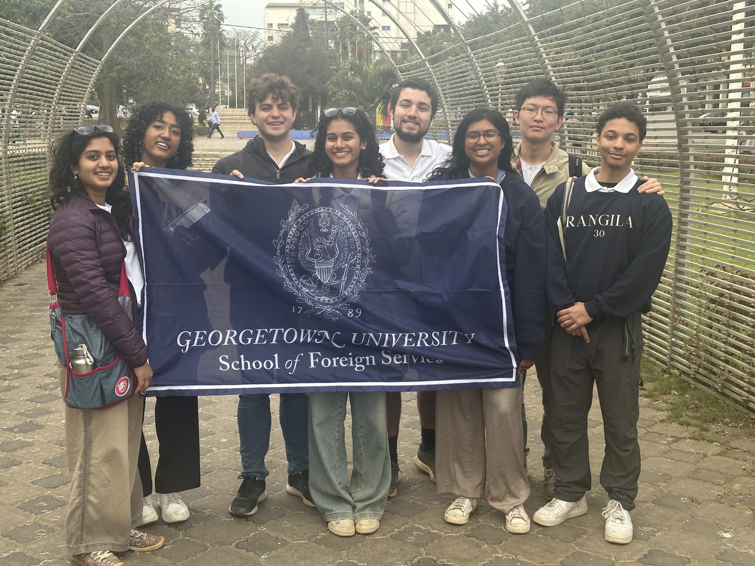 Group of eight students holding a Georgetown University School of Foreign Service banner, standing outdoors.