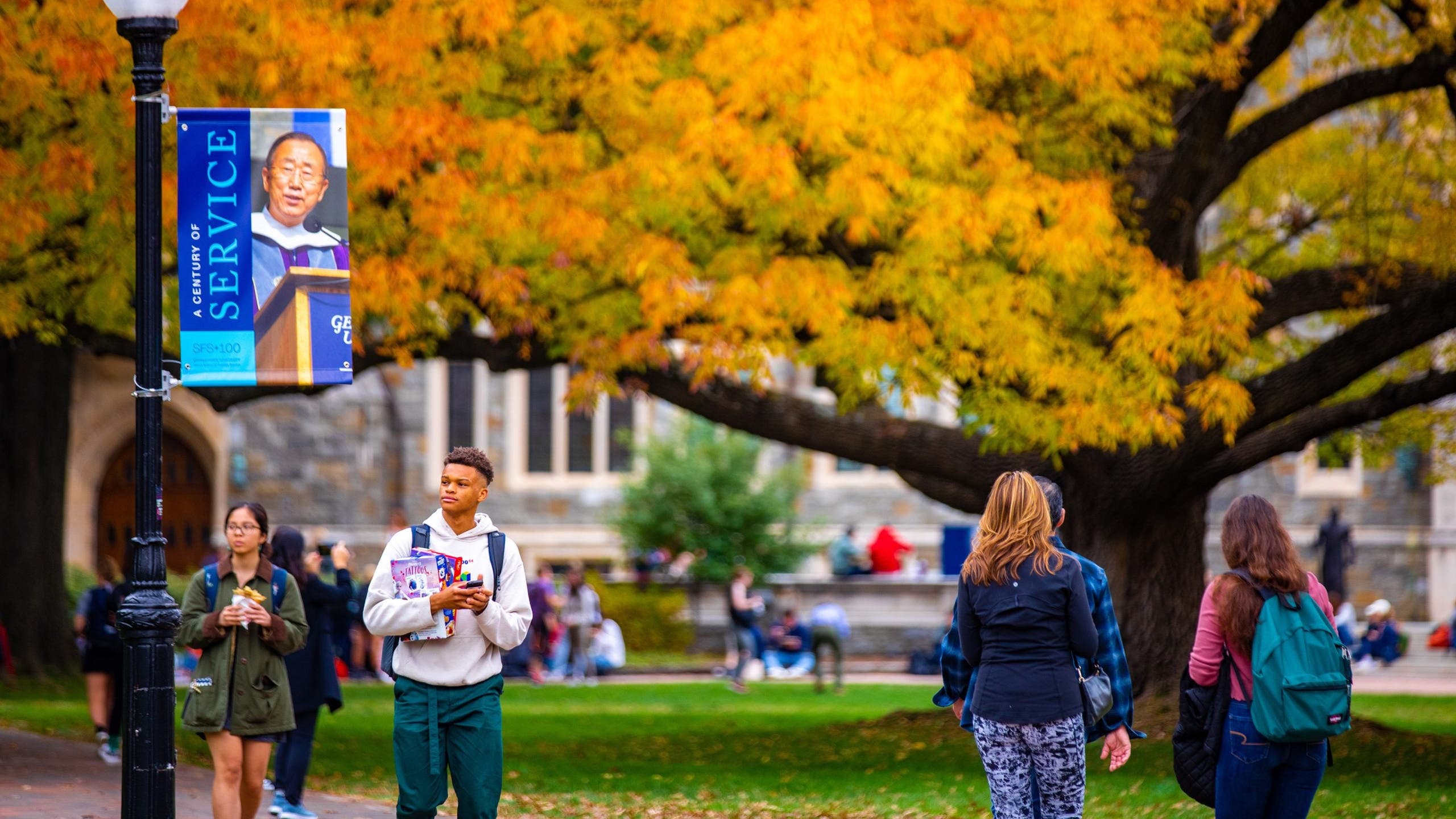 Students walking at the Georgetown campus in the fall. A Tree with orange leaves in the background.