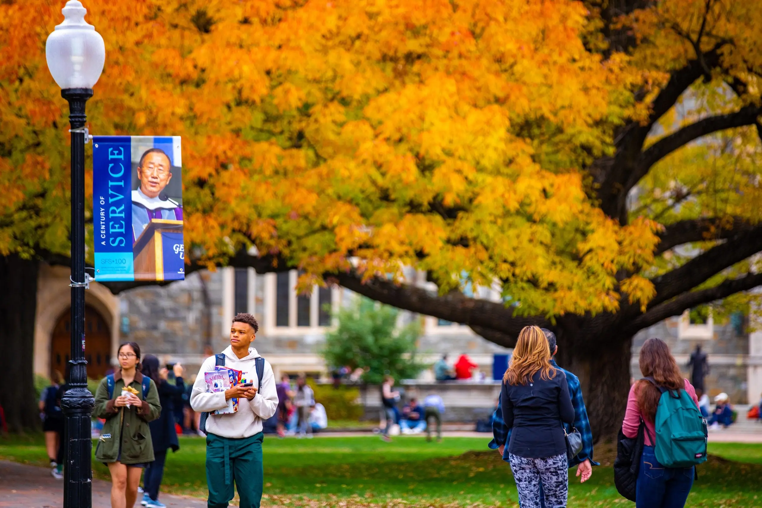 Students walking at the Georgetown campus in the fall. A Tree with orange leaves in the background.
