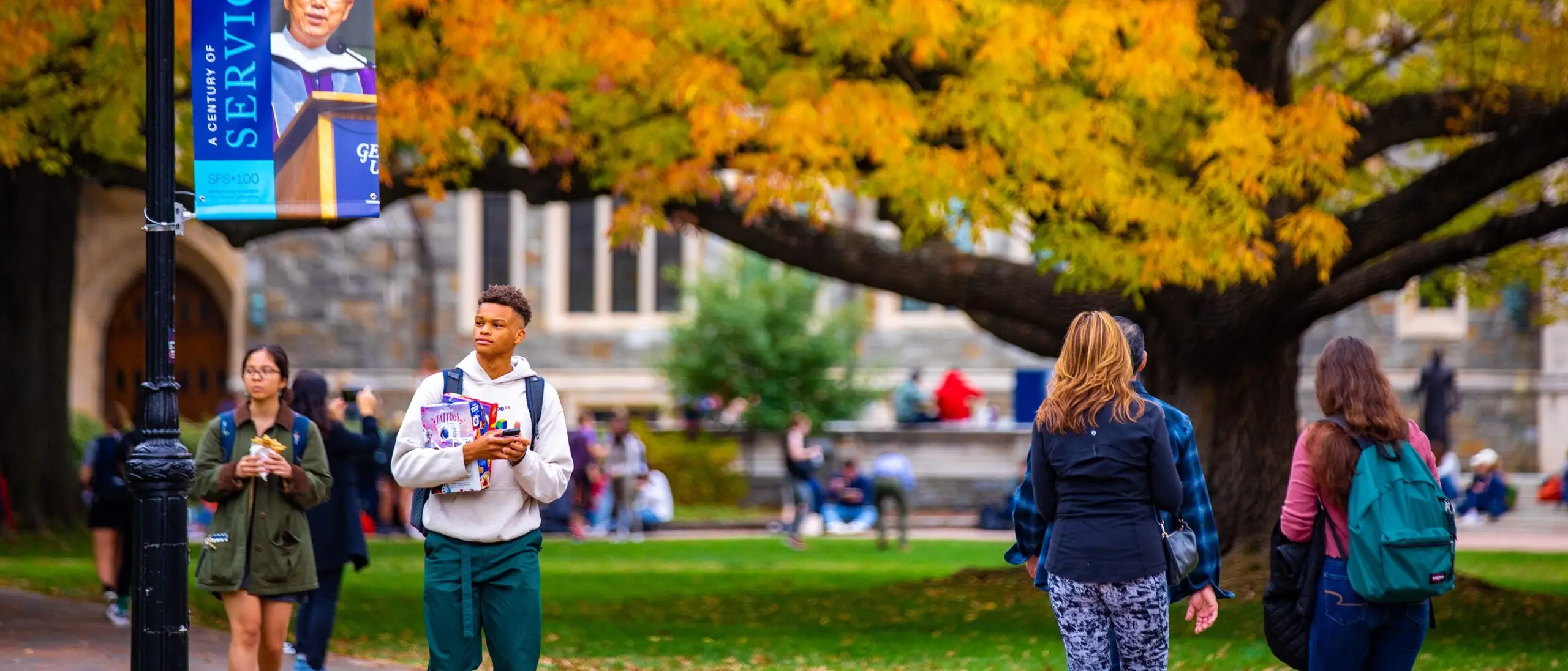 Students walking at the Georgetown campus in the fall. A Tree with orange leaves in the background.