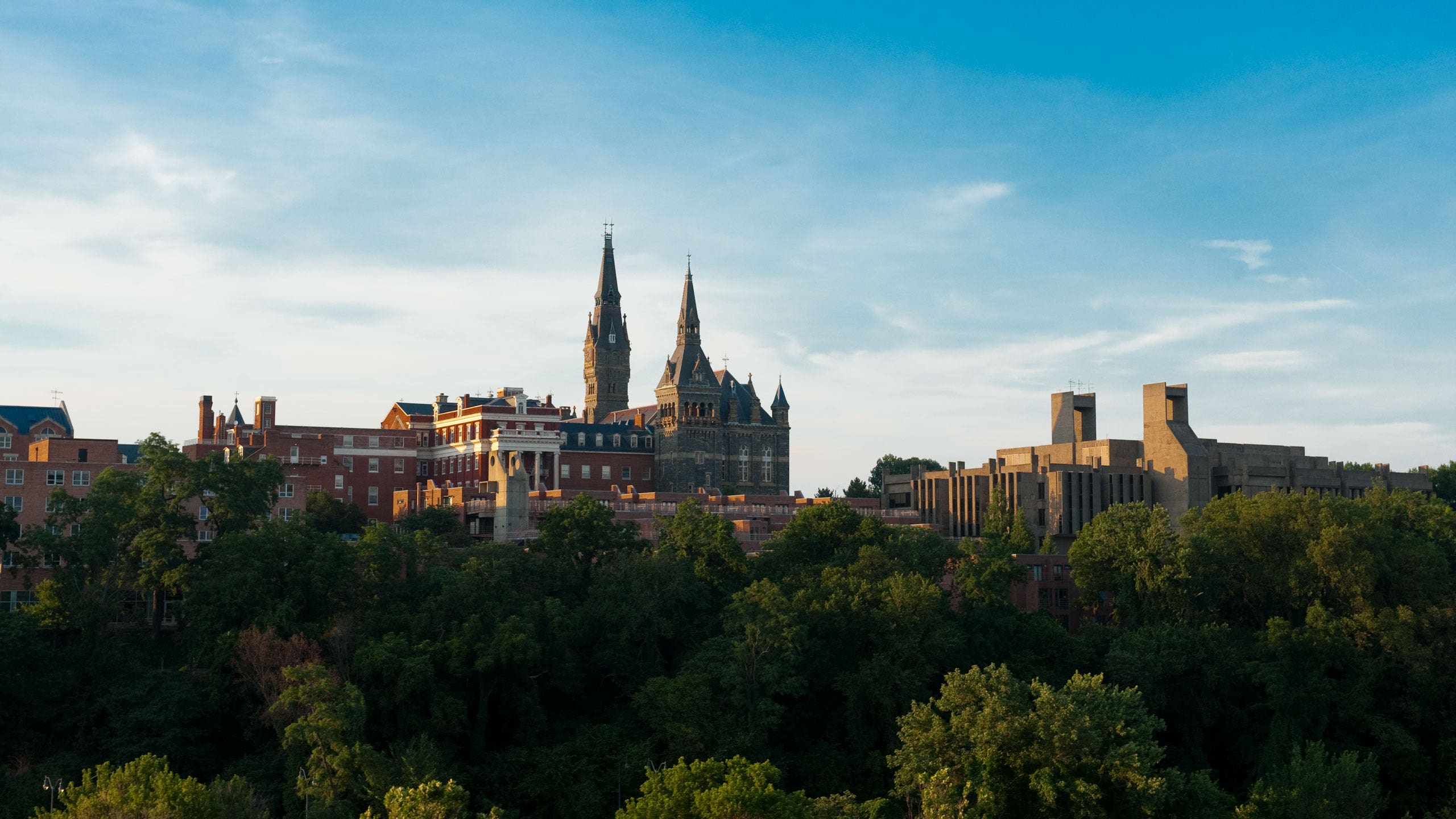 Aerial shot of Georgetown University showcasing Healy Hall, surrounded by green trees, and a bright blue sky