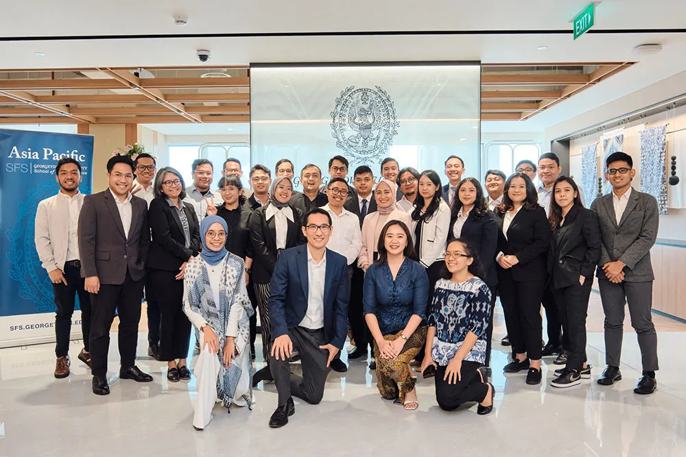 Large group of Asian men and women in front of Georgetown University seal