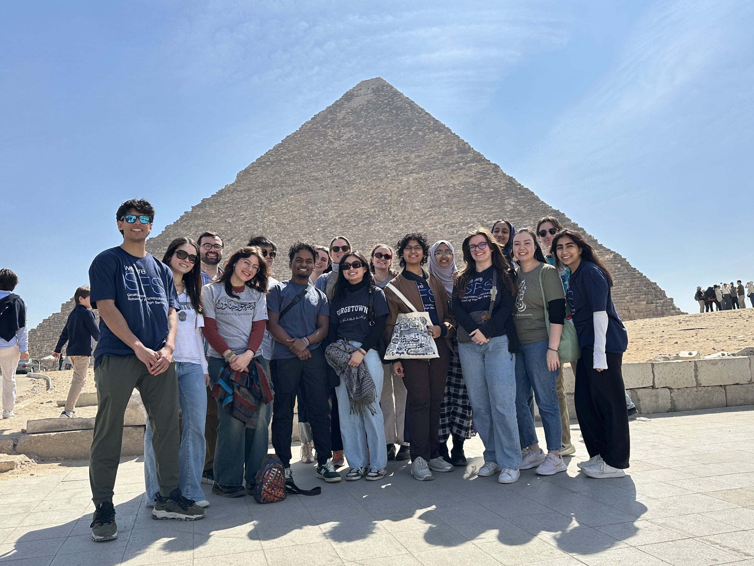 Seventeen college students in casual clothes smile in front of a pyramid in Egypt
