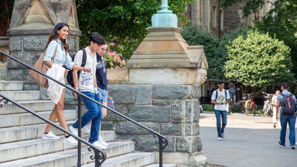 three students going down the Healey stairs smiling in the summer, on a sunny day.