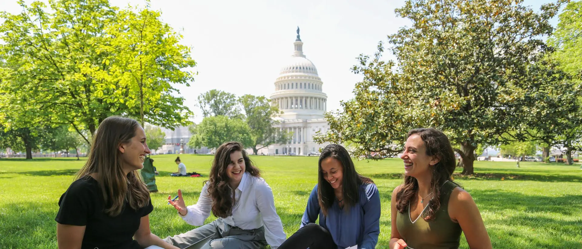 Four students sitting on the US Capitol lawn, talking and studying.