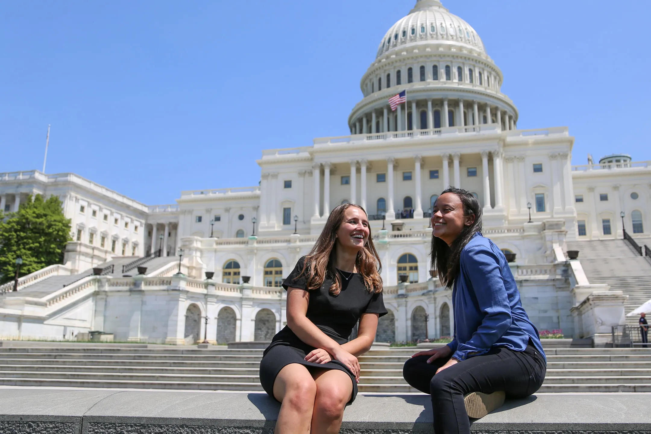 Two young women sitting in the chairs in front of the capitol building smiling while having a conversation.