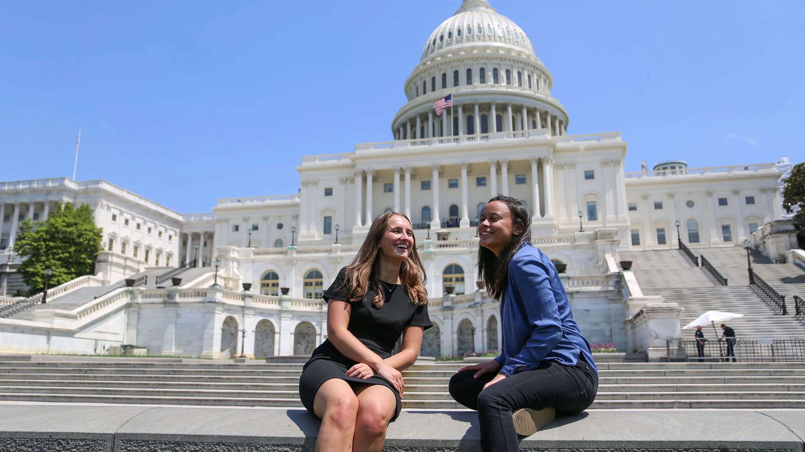 Two young women sitting in the chairs in front of the capitol building smiling while having a conversation.