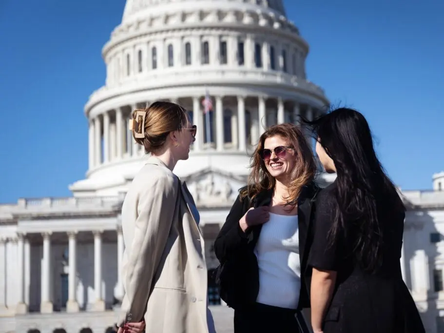 Three students smiling, and laughing in front of the US Capitol building.