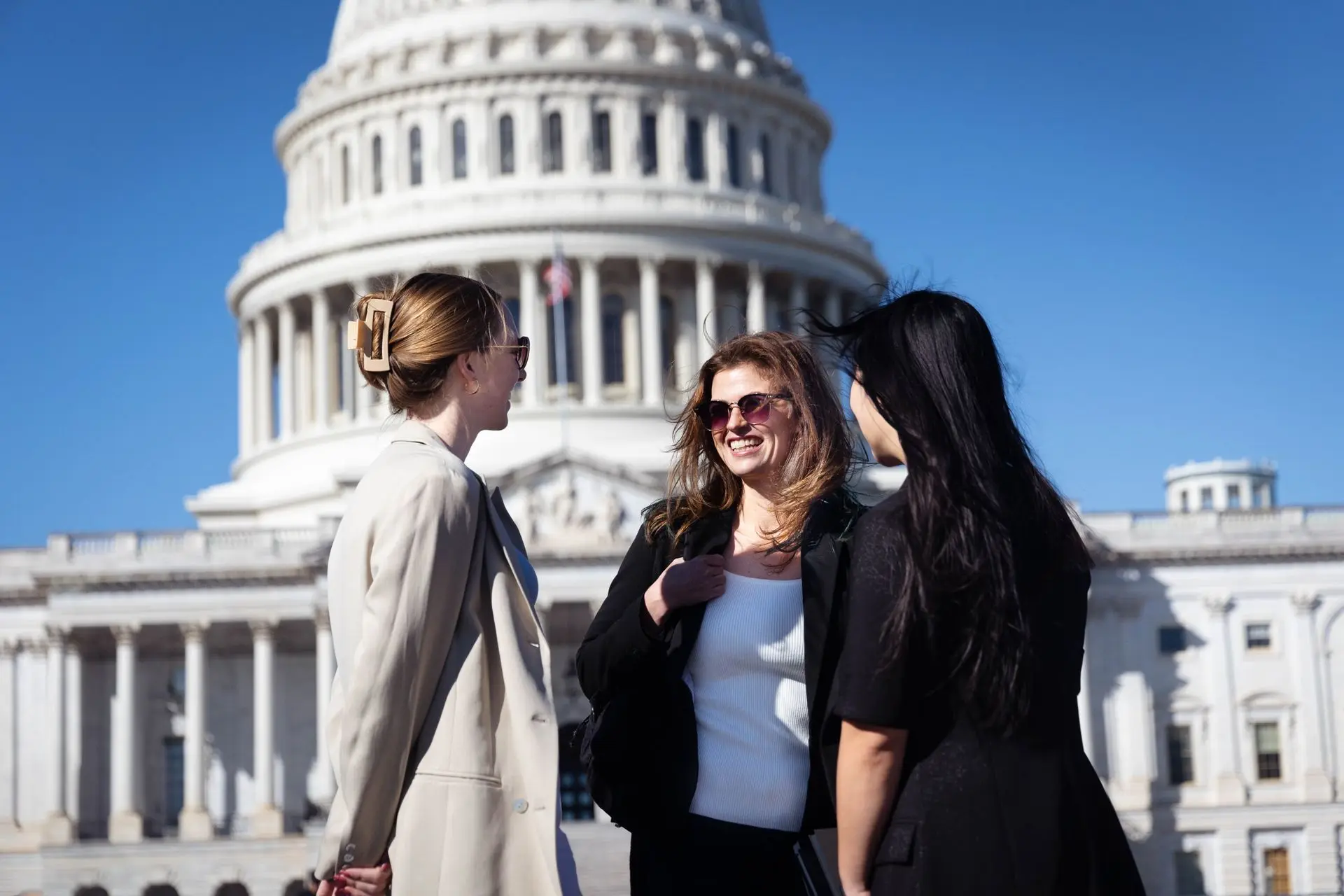 Three students smiling, and laughing in front of the US Capitol building.