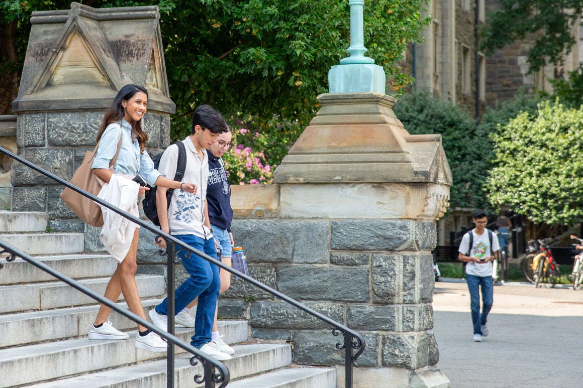 three students going down the Healey stairs smiling in the summer, on a sunny day.