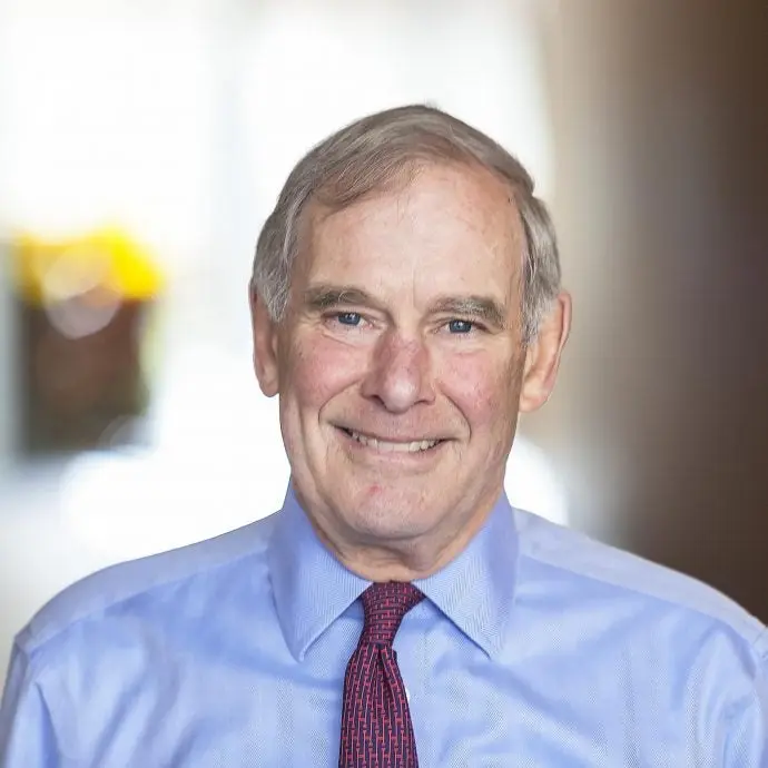 A man with grey hair in a light blue dress shirt wiht a red and blue tie