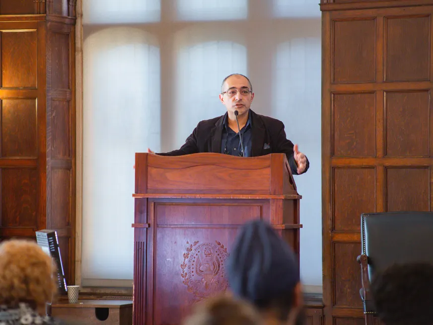 Nader Hashemi wearing a suit, speaking in front of an audience, on a wooden podium with the Georgetown crest.