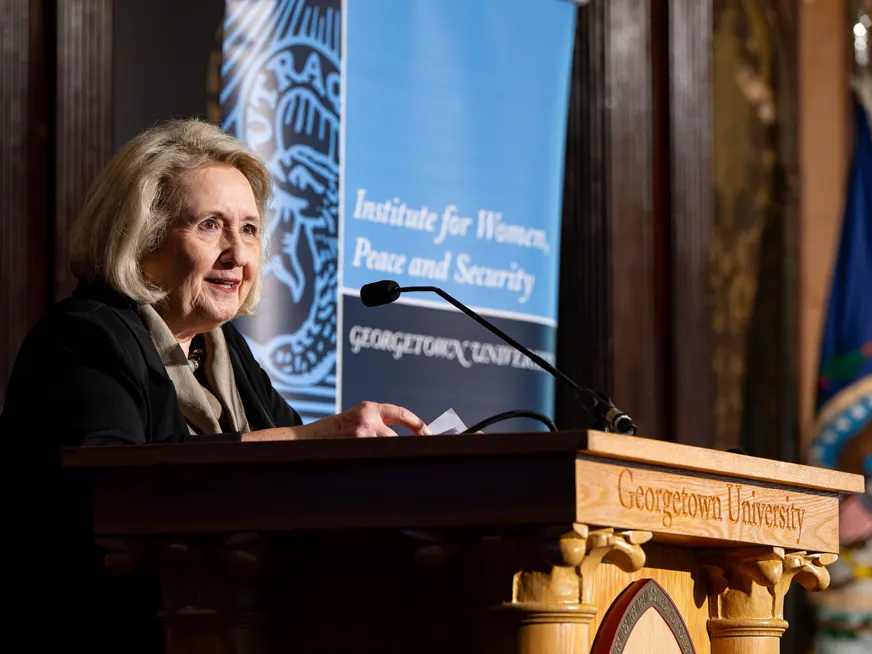 Ambassador Verveer speaking on a Georgetown podium, behind her a banner for the Institute for Women, Peace and Security