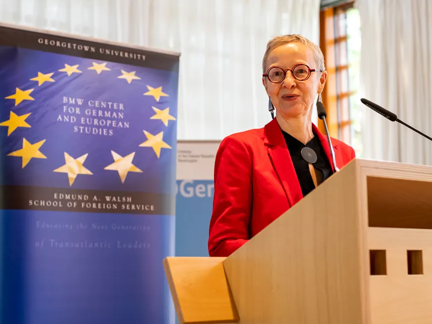 A woman speaking on a podium, behind her a banner for the BMW Center for German and European Studies. The banner has the European Union circle of stars.