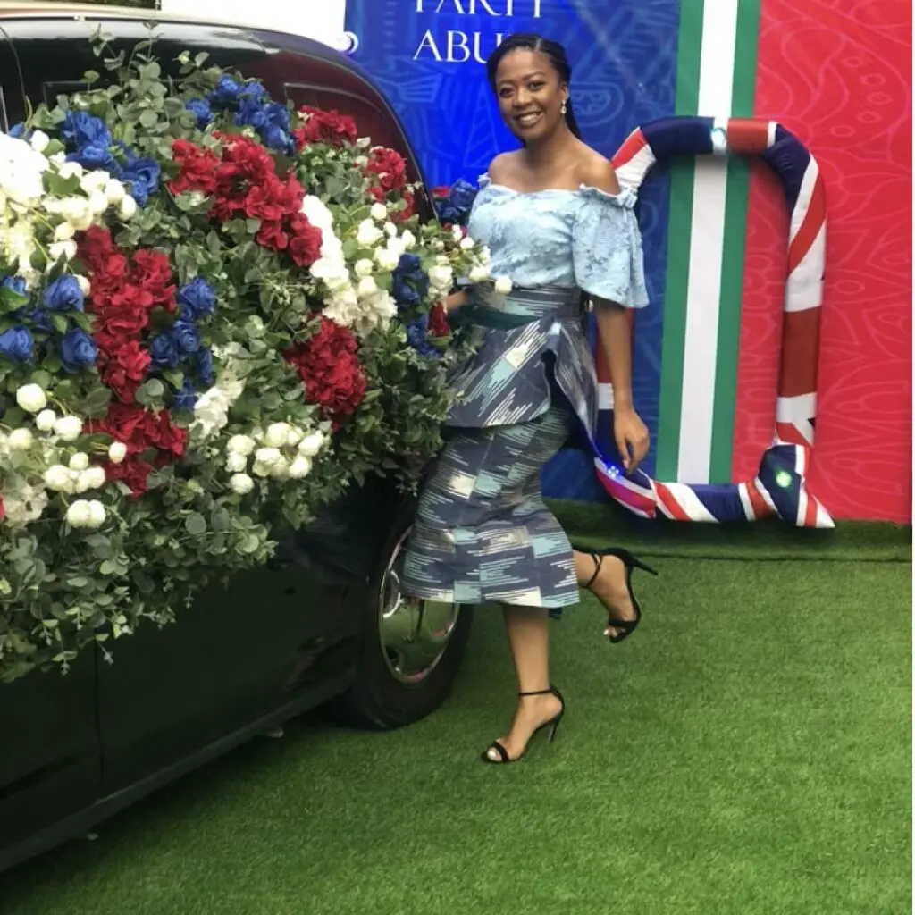 Georgina Mugugu wearing a pattern dress standing in front of a car covered in flowers.