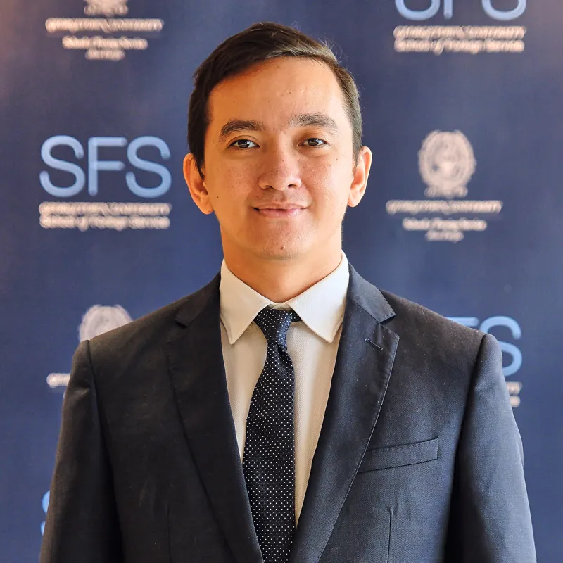 Headshot of Guilford Caesar, in front of a backdrop with the Georgetown and School of Foreign Service logo.