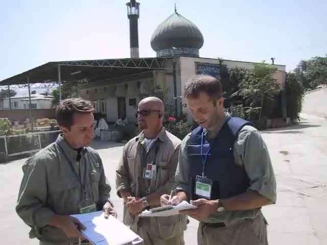 Three individuals in military-style clothing and badges reviewing documents in front of the Abu Hanifa Mosque in Baghdad.