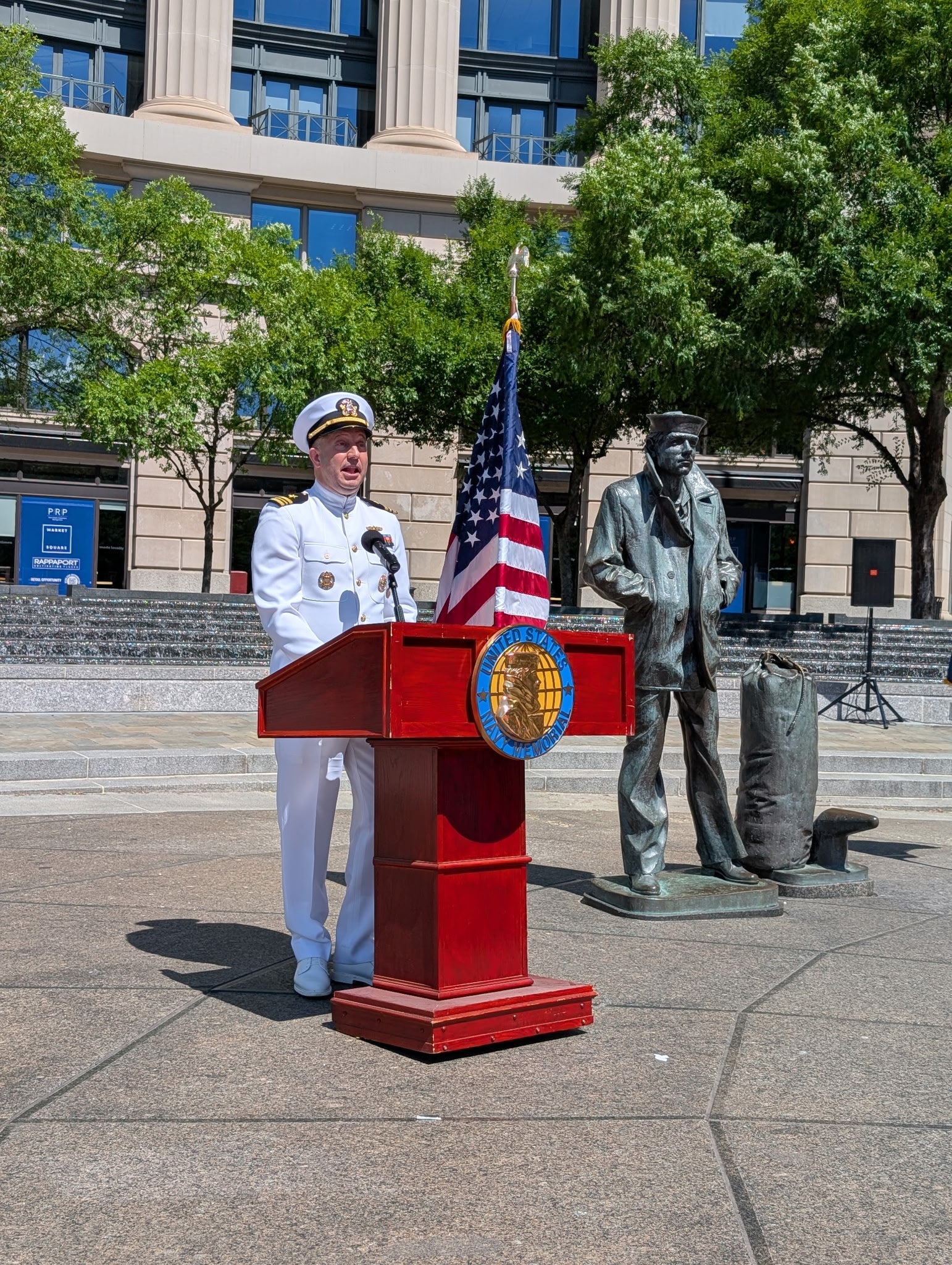 A person in a white naval uniform is giving a speech at a podium.