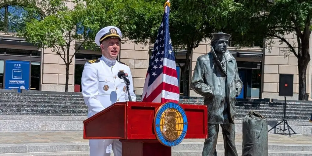 A person in a white naval uniform is giving a speech at a podium.
