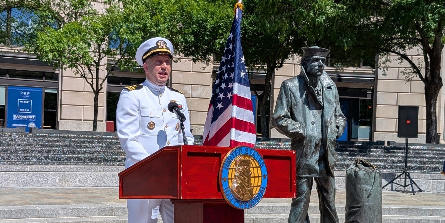 A person in a white naval uniform is giving a speech at a podium.