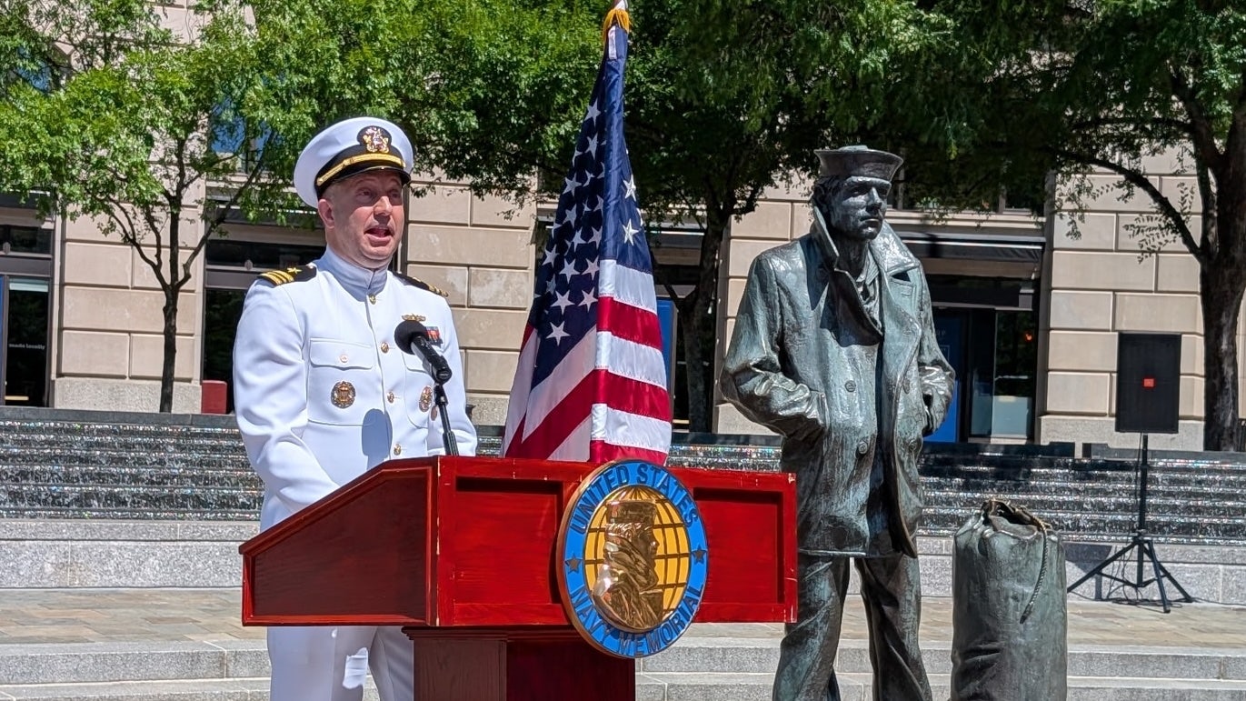 A person in a white naval uniform is giving a speech at a podium.