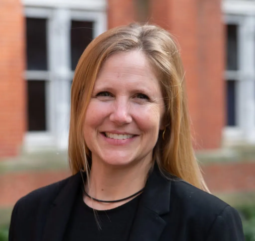 A headshot of a blond woman wearing a black suit jacket and black shirt