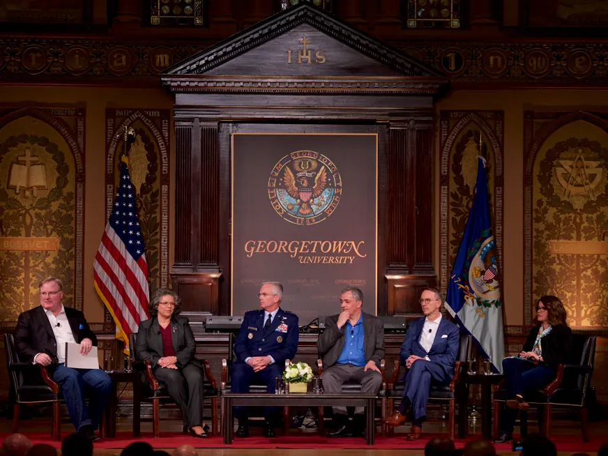 Six people in a panel, two women and four men, all in business attire, and one in uniform with medals.