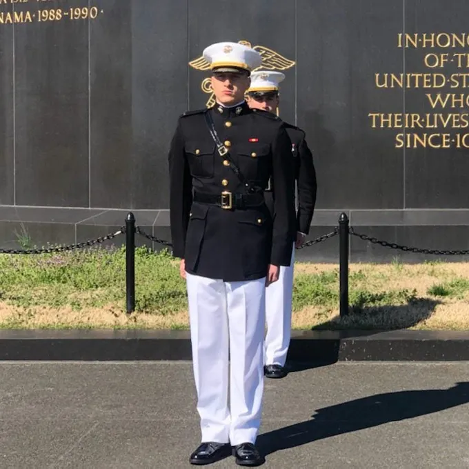Eosin Chelius standing in uniform, with white pants, and a black buttoned up shirt, and a white hat.