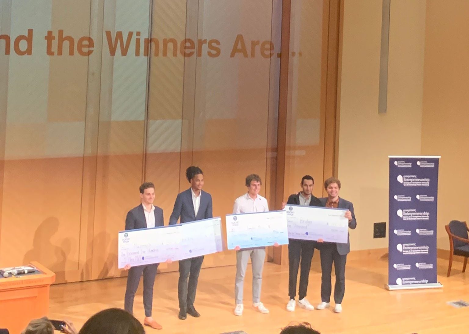 Photo of students holding award checks. From left to right three students are holding three different checks and two students are holding one check.