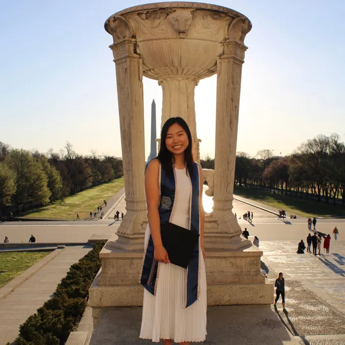 Grace Hyemin smiling with a gratuation cap in her hand. Behind her the Washington monument.