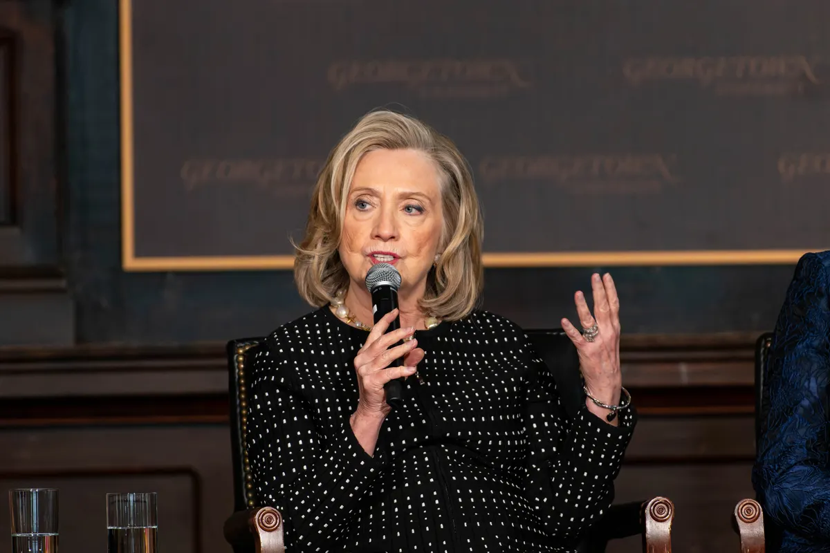 Hilary Clinton speaking at a panel, she is sitting down, behind her a wall with the Georgetown University logo