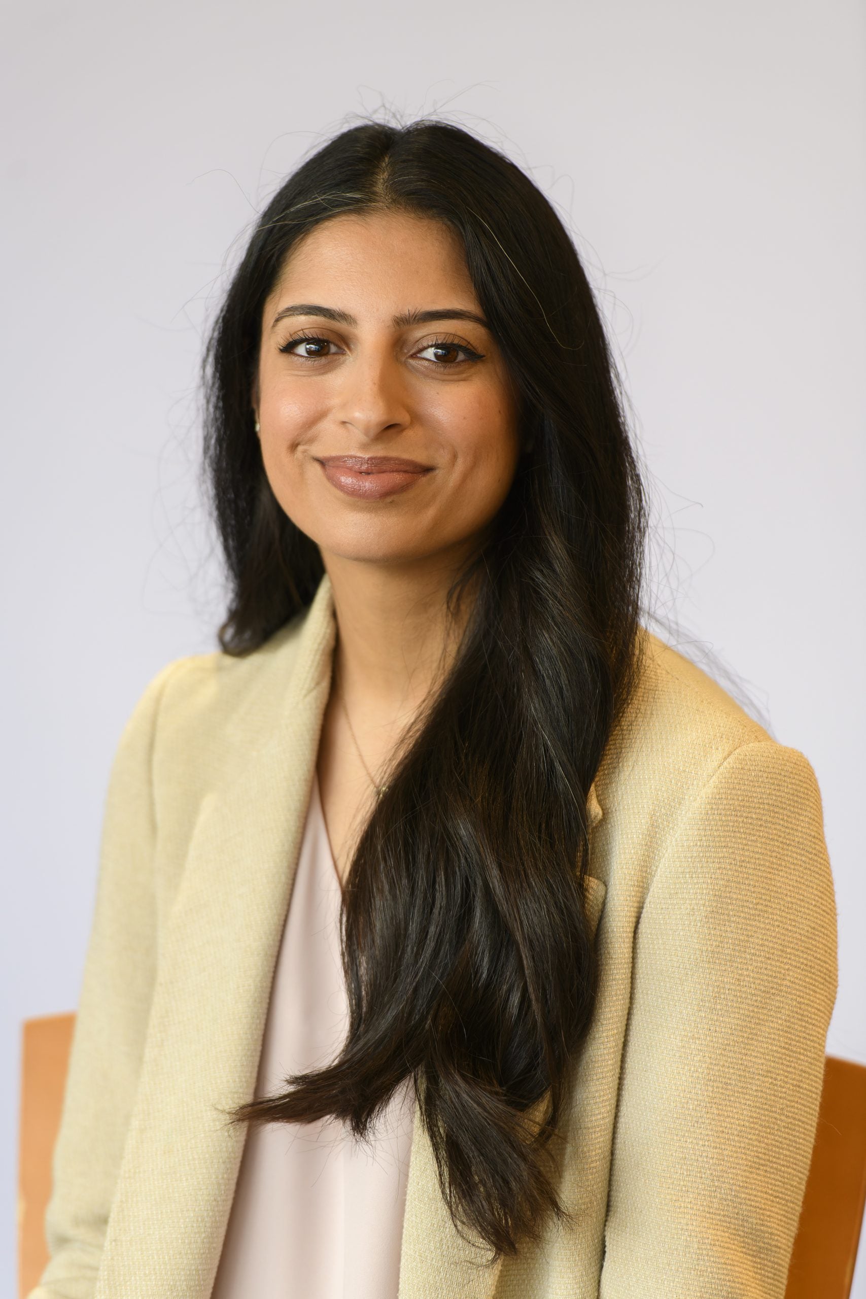 Headshot of Aliya Iftikhar smiling, wearing a yellow blazer.