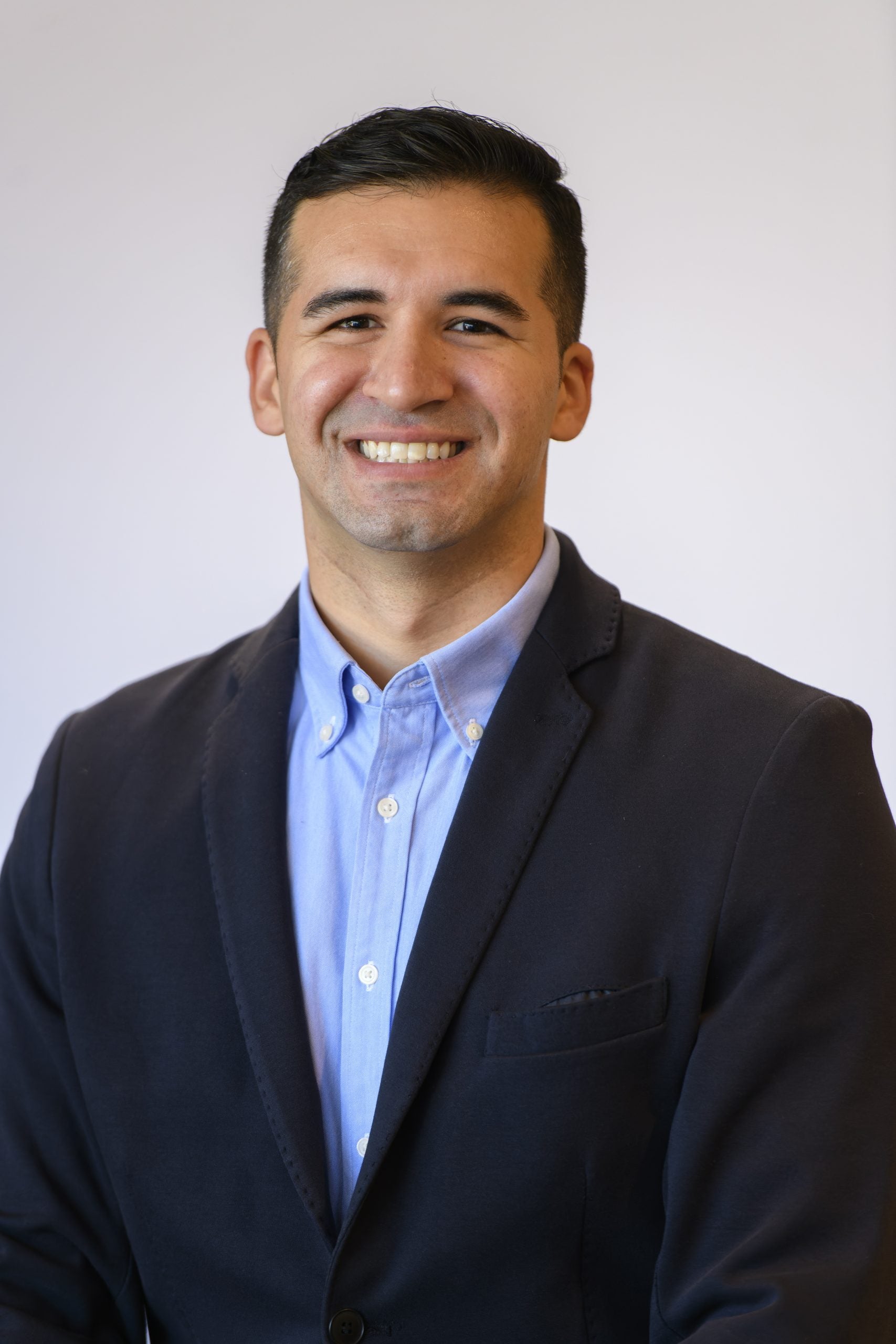 Headshot of Michael Rea smiling, wearing a blue shirt underneath a black blazer.