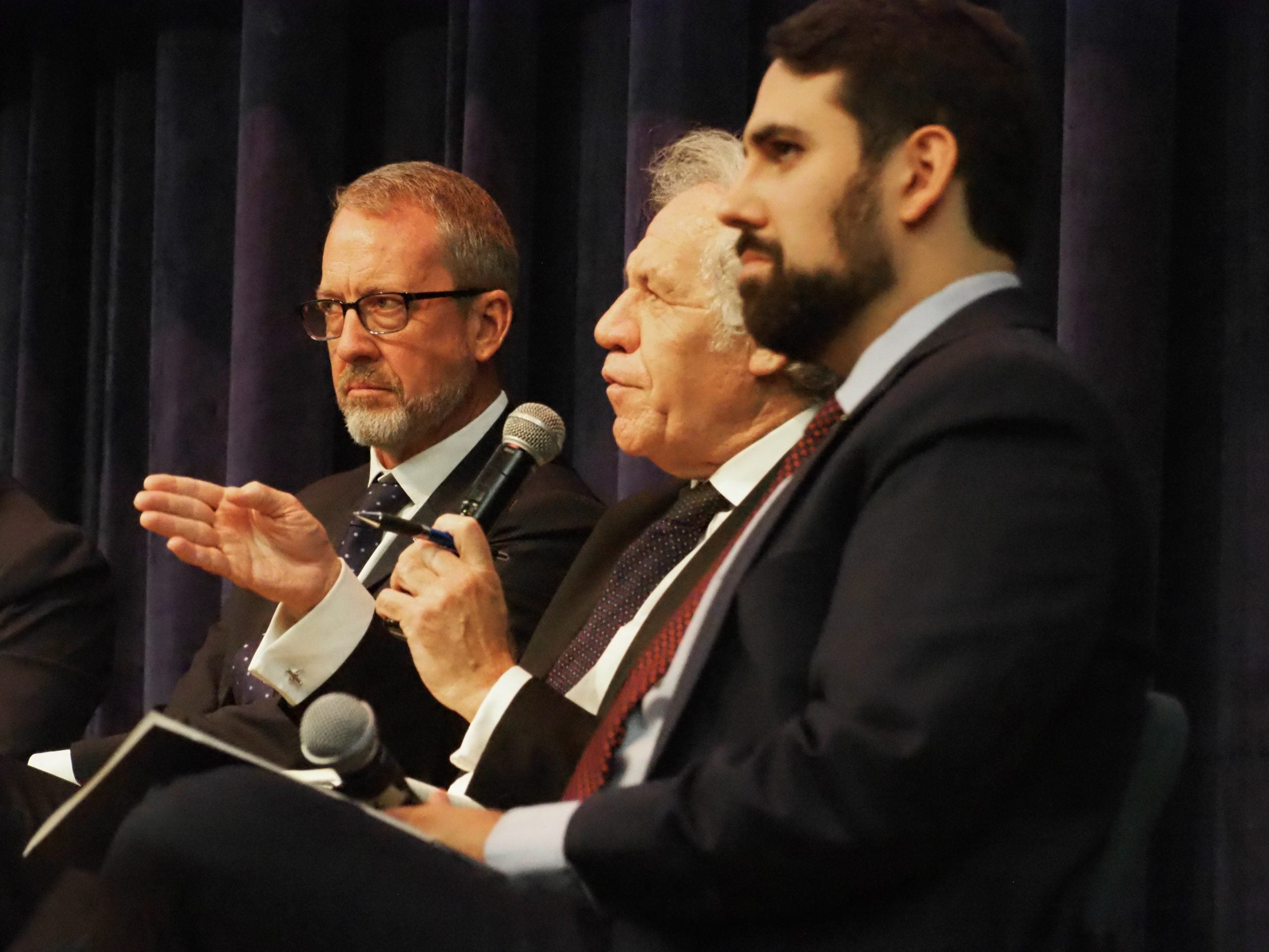 Photo of three panelists sitting. Secretary General Almargo, sitting in the middle, is answering questions, holding a microphone.