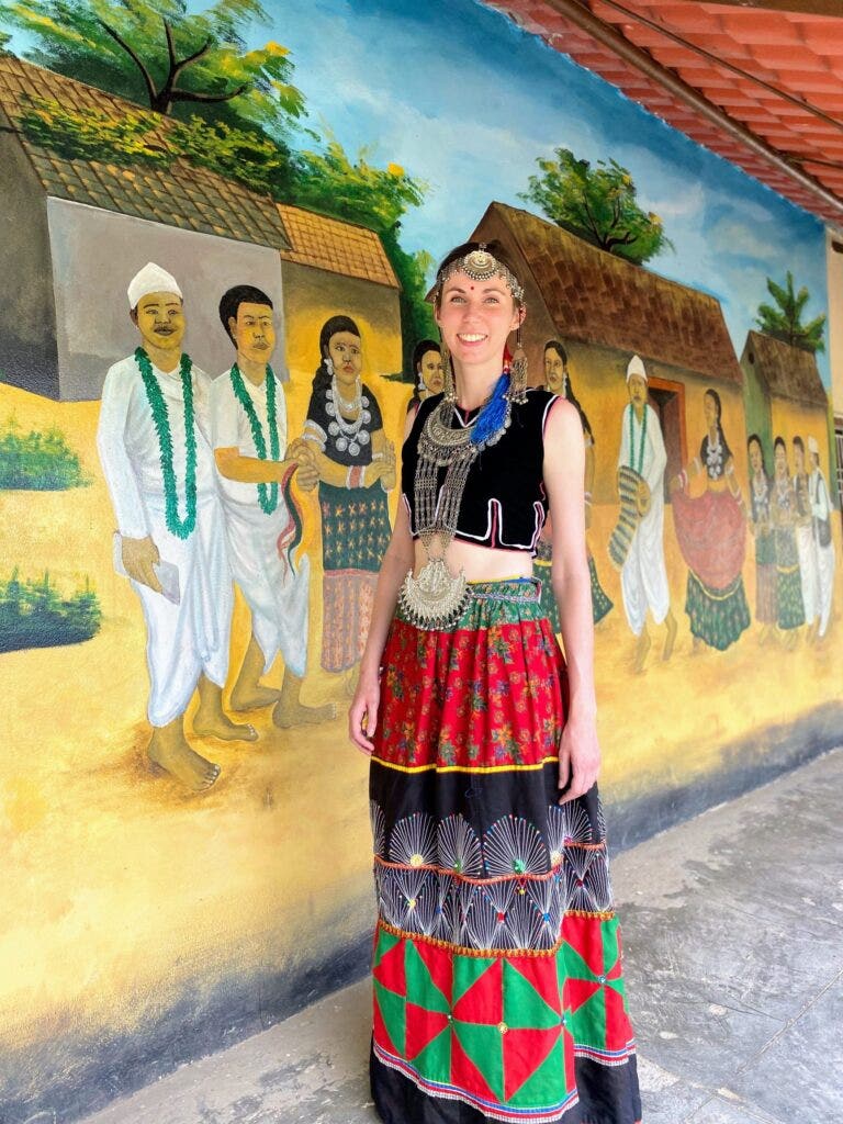 Therese in a traditional Tharu dress, posing in front of a mural.