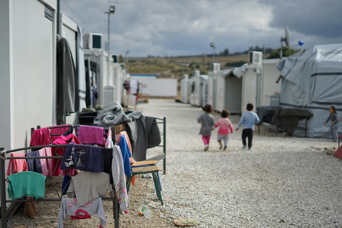 cloudy day, camp site, three children walking, holding hands. Clothes handing on chairs.