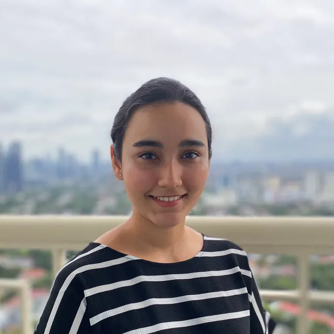 Headshot of Sargun Kaur smiling. Behind her the landscape of a city.