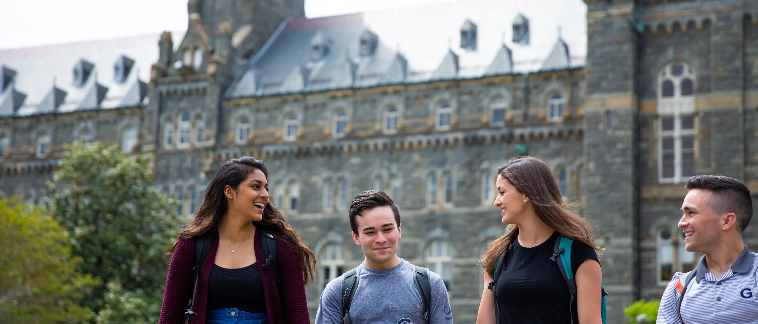 Four students walking on the Georgetown University campus, they are smiling and in conversation with each other.