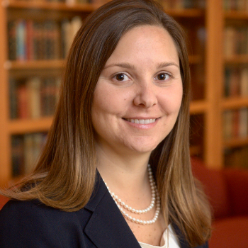 A woman with long brown hair, a double string of pearls, and a navy jacket.