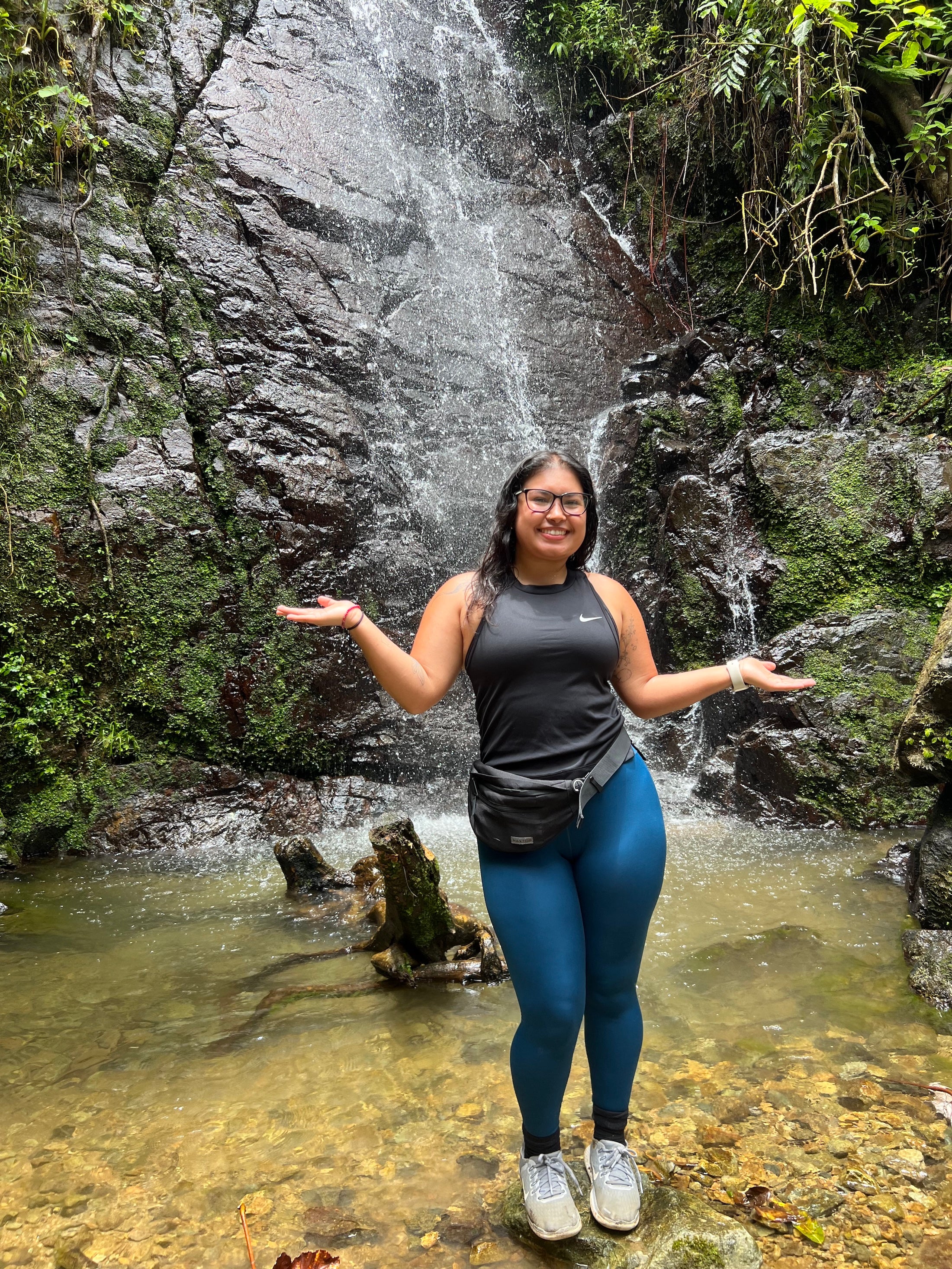 Priscila standing on a rock in front of a waterfall, smiling