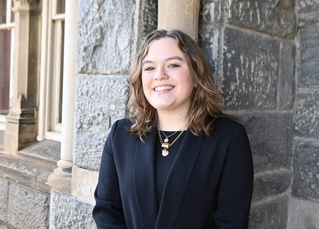 Woman with short hair wearing a black blazer smiling in front of a stone building.