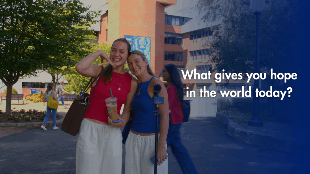 Two individuals smiling and interacting on a university campus, one holding a beverage, with the text "What gives you hope in the world today?" overlaying the image.