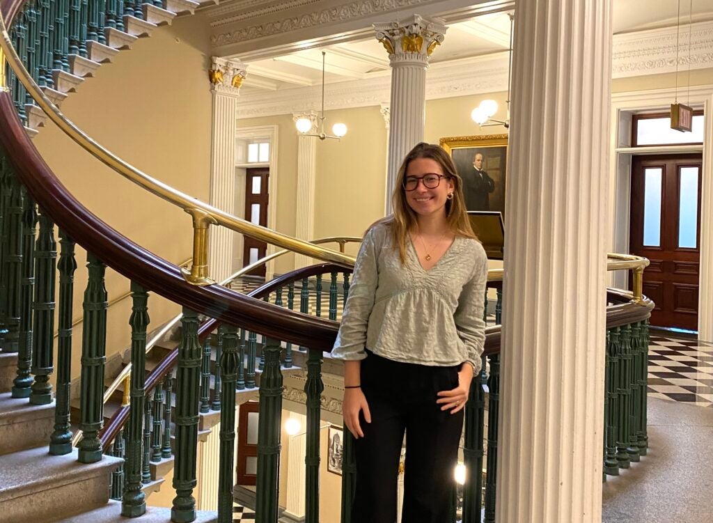 A person standing at the base of the ornate spiral staircase. The staircase features elegant green railings and white columns.