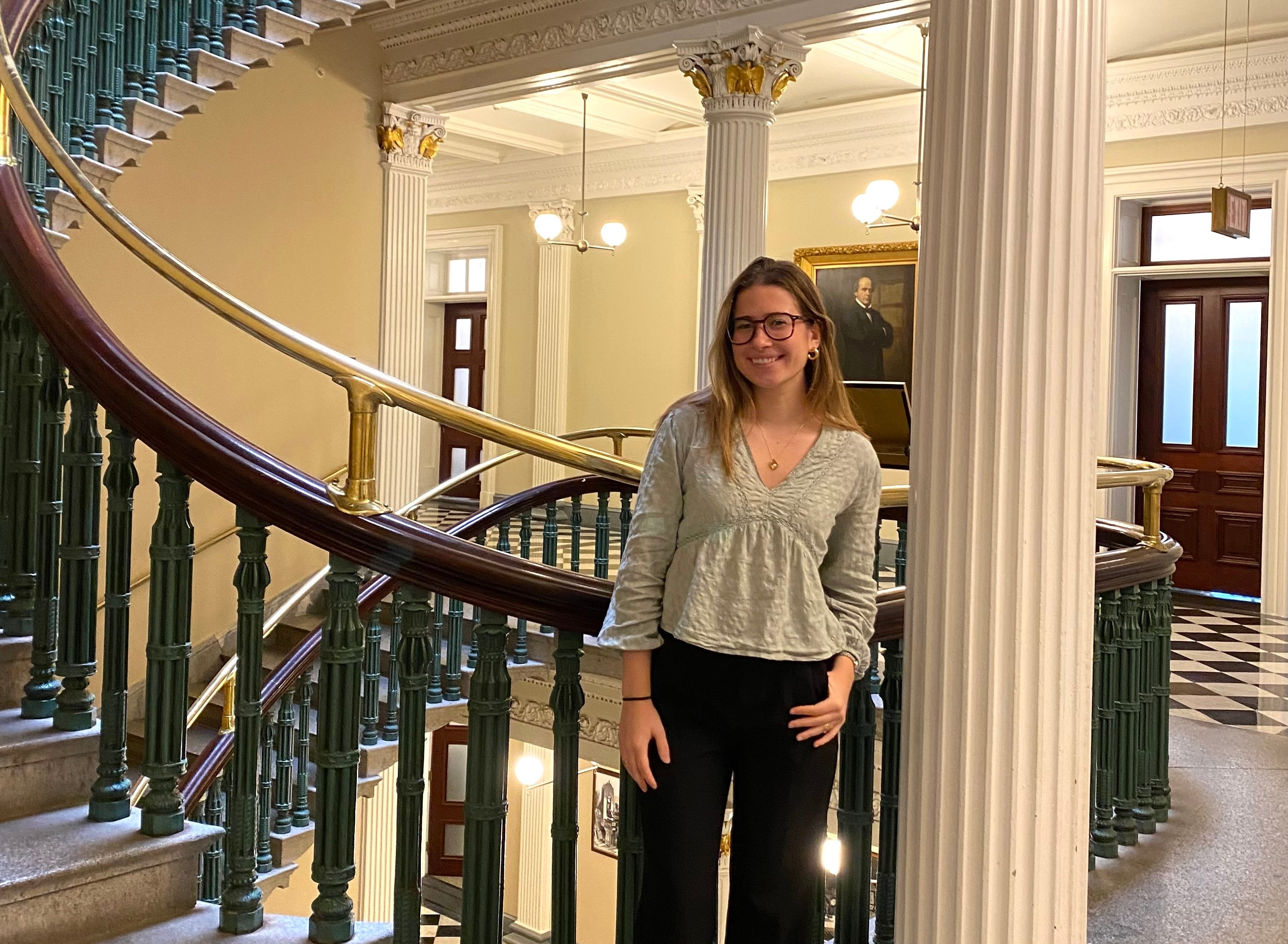 A person standing at the base of the ornate spiral staircase. The staircase features elegant green railings and white columns.