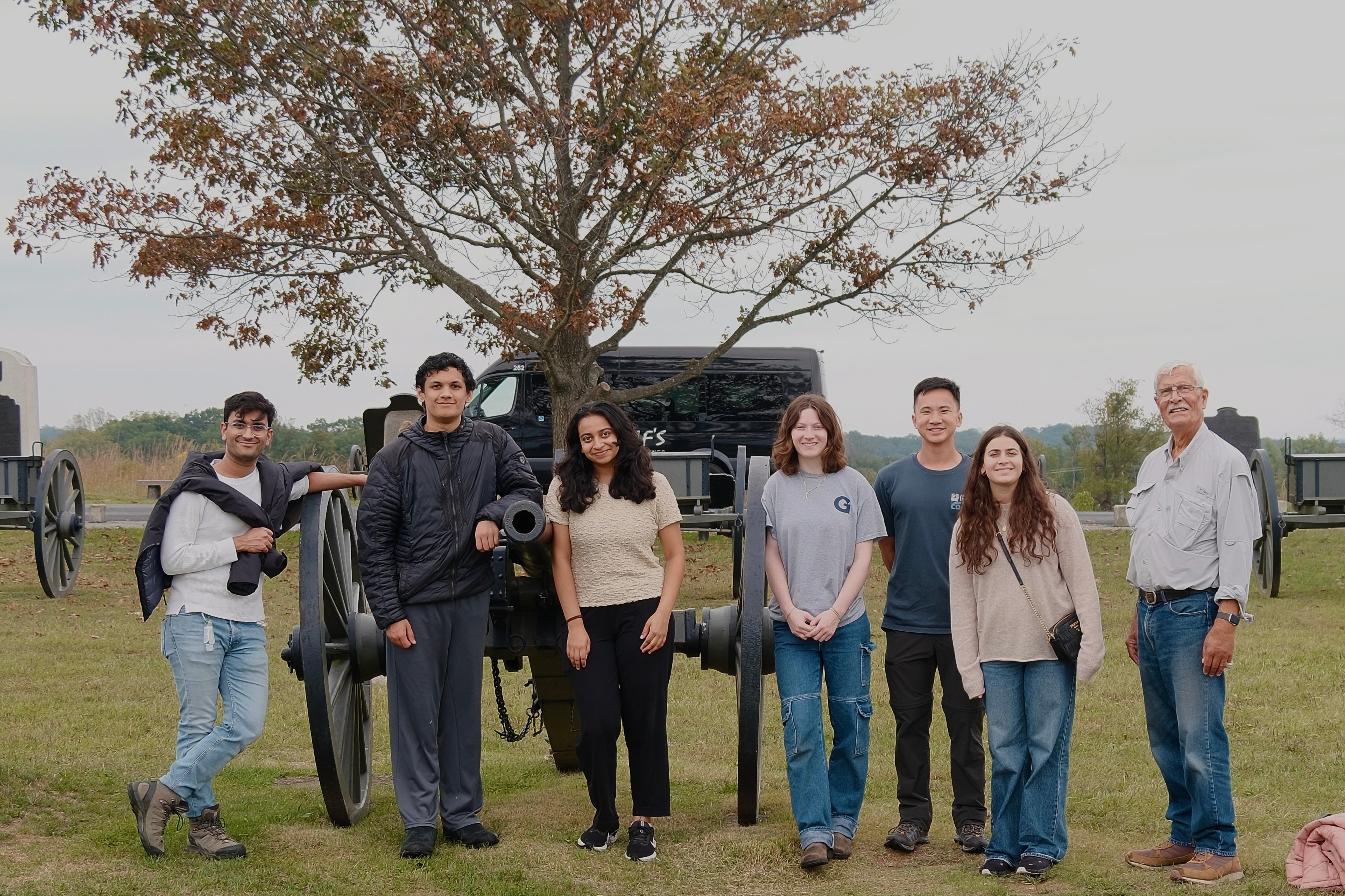 Professor McNaugher and six students stand in front of a cannon at Gettysburg. They stand in a line, smiling at the camera for a group photo.