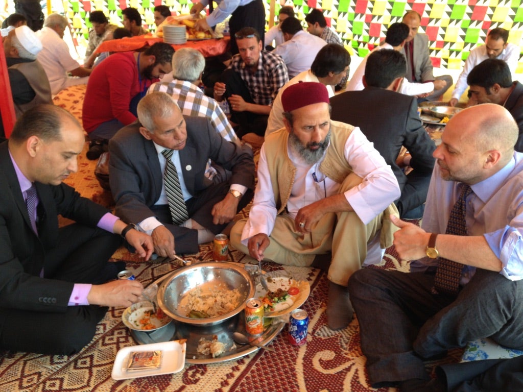 Several individuals gathered around a large dish of food, engaging in conversation at a cultural event.