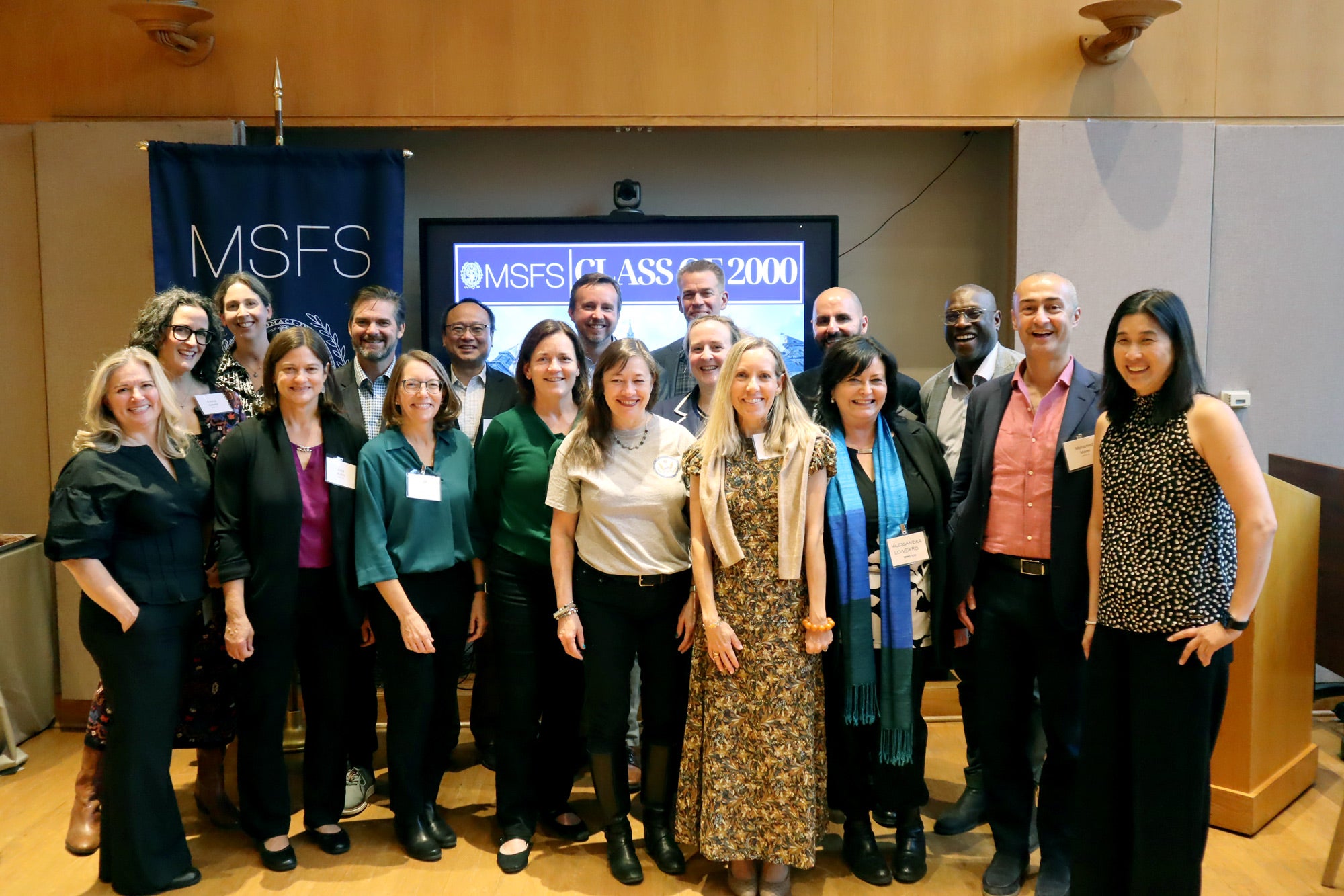 18 people standing together, smiling, in front of a screen that says "MSFS Class of 2000"