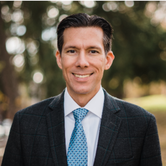 Headshot of Professor Paul Miller smiling, wearing a black suit with a blue tie